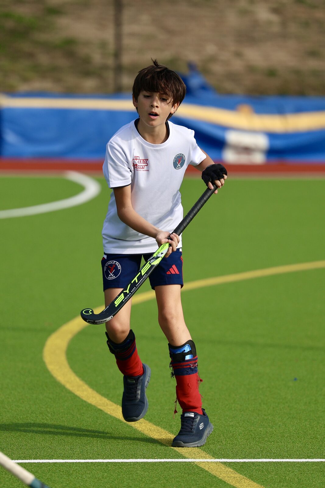 A young player in the white bib surveys the pitch, stick ready