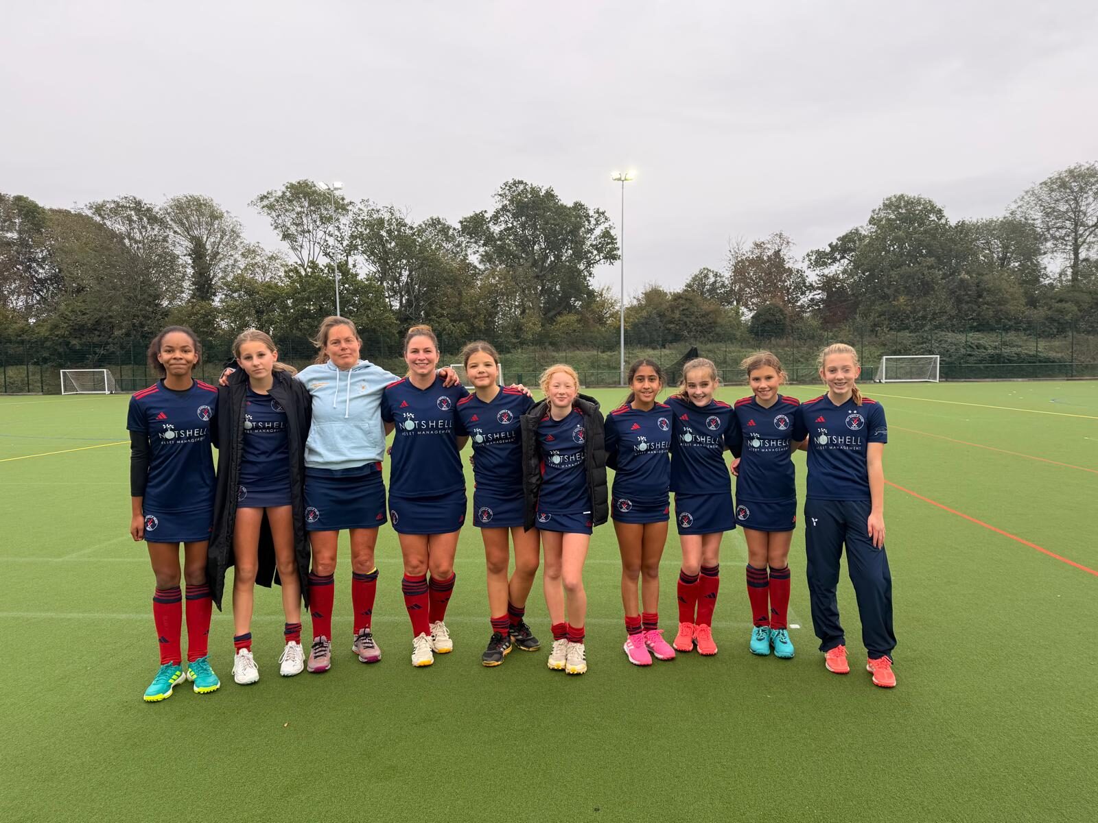 The HC Knole Park Women's 2s squad lined up arm in arm on the pitch after their win over Holcombe