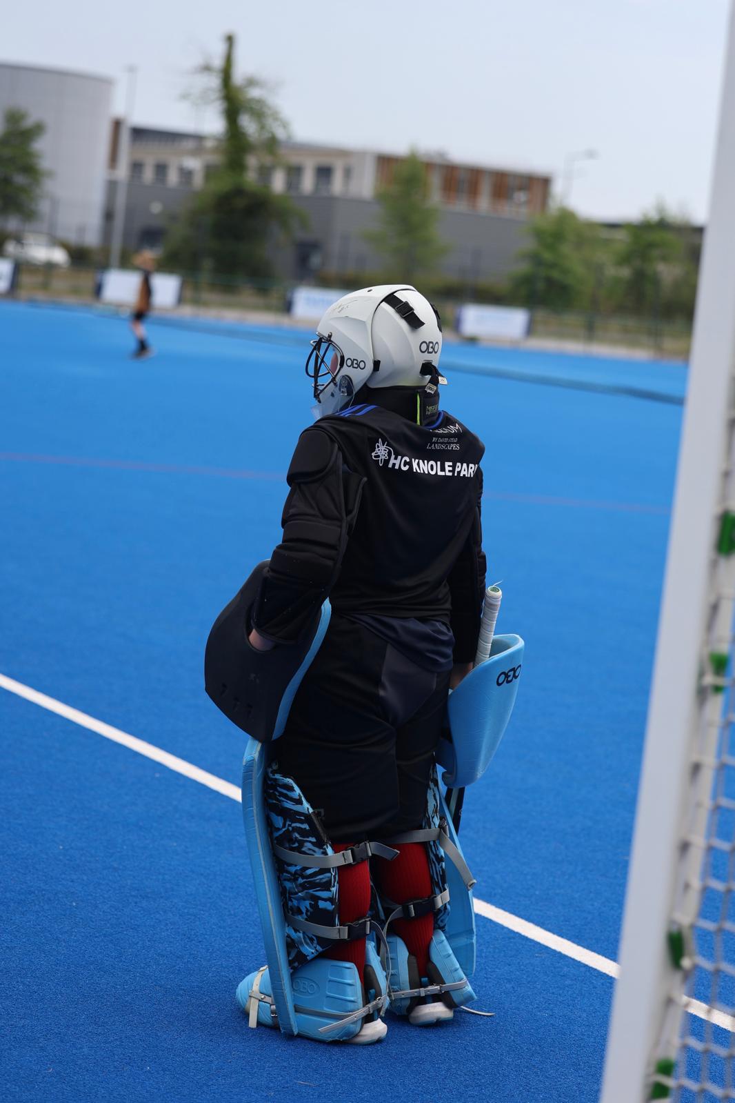 Junior keeper in full protective kit watching play from the goalpost
