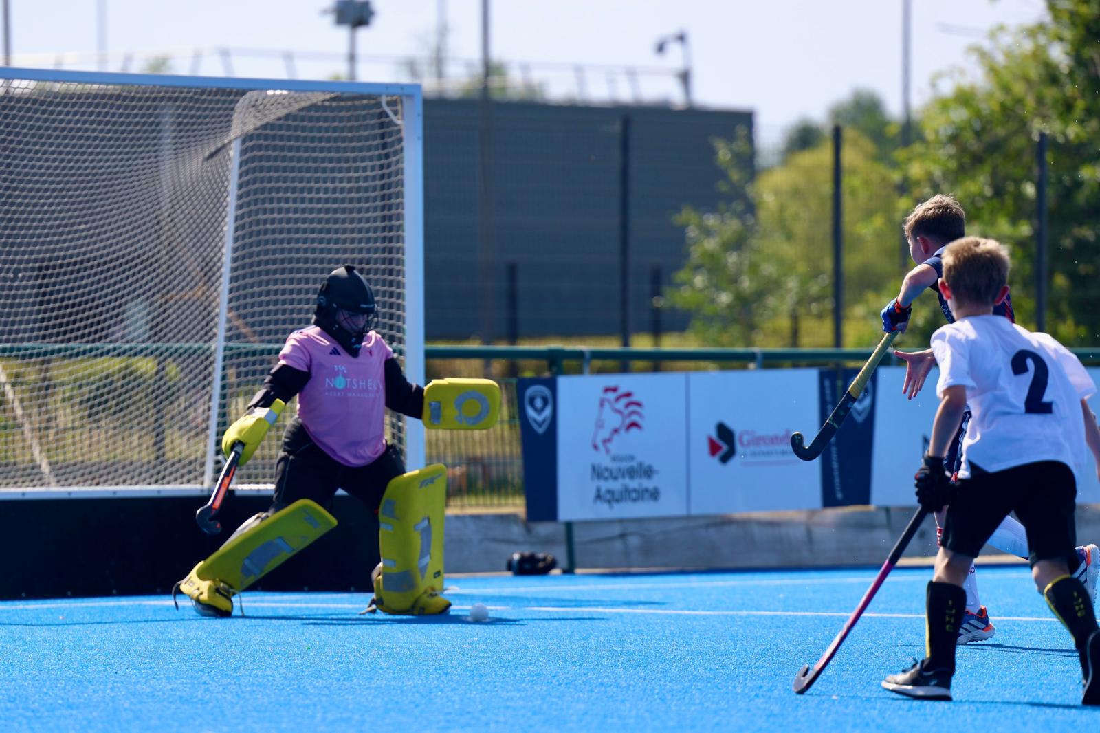 A young HC Knole Park goalkeeper in pink and yellow kit makes a save in a match