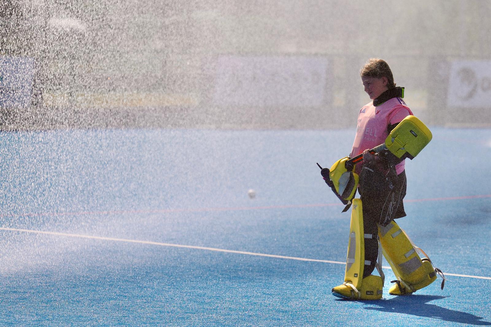 HC Knole Park goalkeeper walking out through the pitch sprinklers